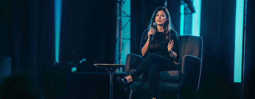 Une femme assise dans un fauteuil tenant un micro pour donner une conférence 